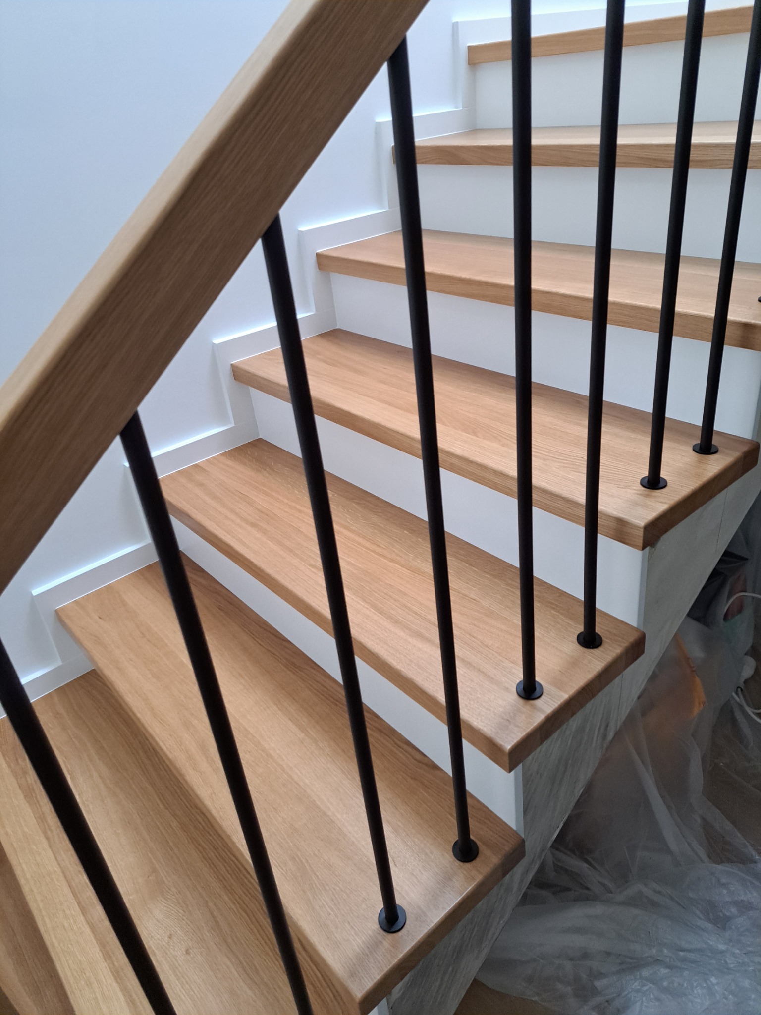 Schody drewniane z jasnego drewna z czarnymi, metalowymi balustradami, widok z góry, zabezpieczone folią malarską.