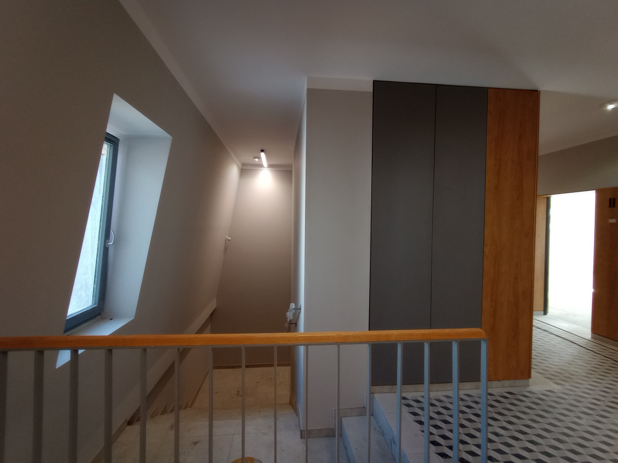 Nowoczesne wykończenie klatki schodowej w Wieluniu: szara kolorystyka ścian, drewniane akcenty i geometryczny wzór posadzki.