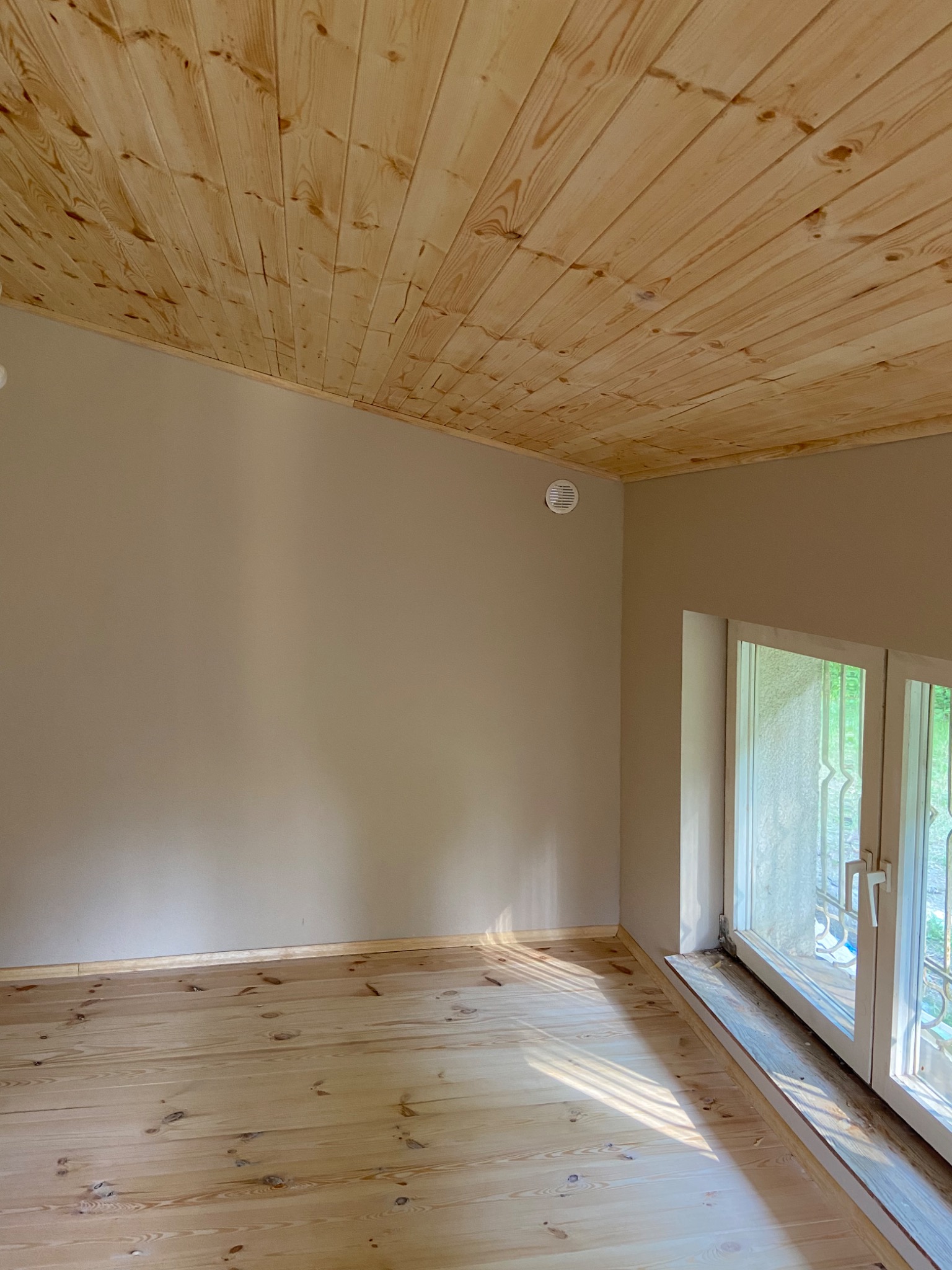 Jasne drewniane panele na podłodze i suficie w pokoju z beżowymi ścianami i białym oknem