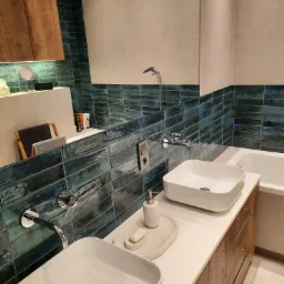 Nowoczesna łazienka z dwiema kwadratowymi umywalkami nablatowymi, drewnianą szafką pod umywalką i turkusowymi płytkami na ścianie.