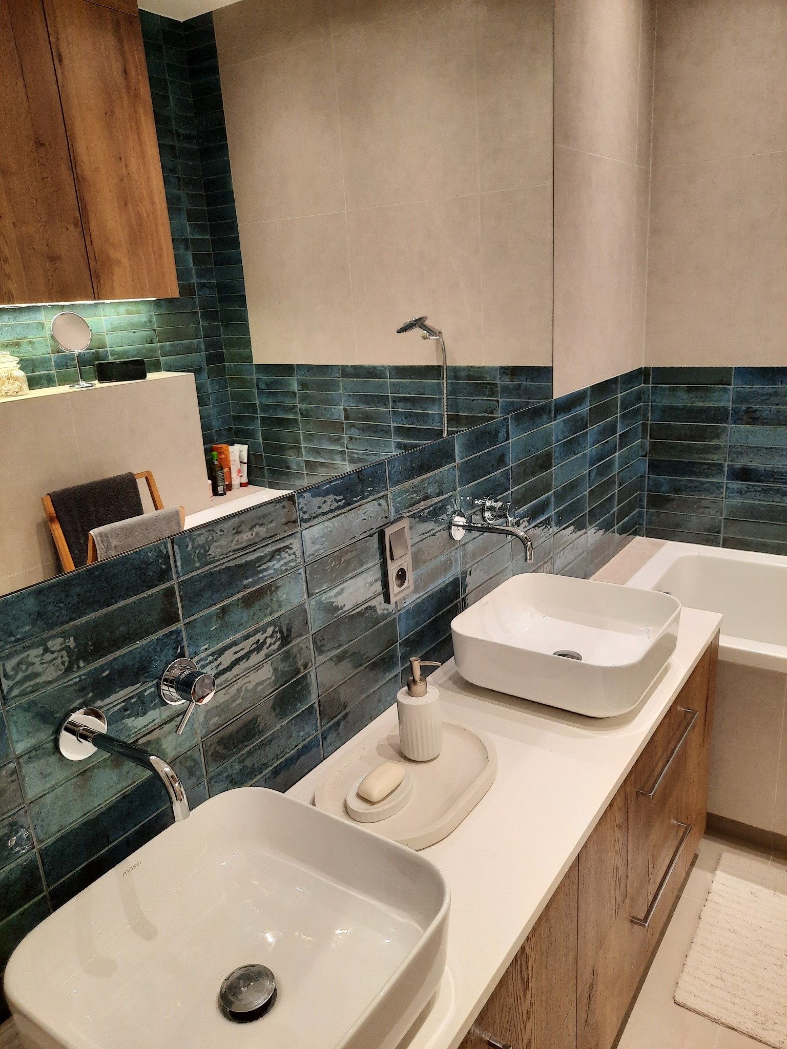 Nowoczesna łazienka z dwiema kwadratowymi umywalkami nablatowymi, drewnianą szafką pod umywalką i turkusowymi płytkami na ścianie.