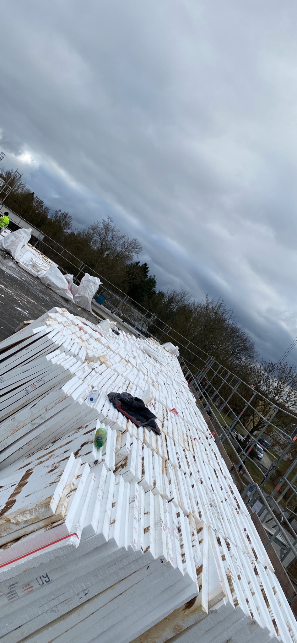 Styropianowe płyty izolacyjne ułożone na dachu budynku w trakcie prac budowlanych, widoczne rusztowania i pochmurne niebo.