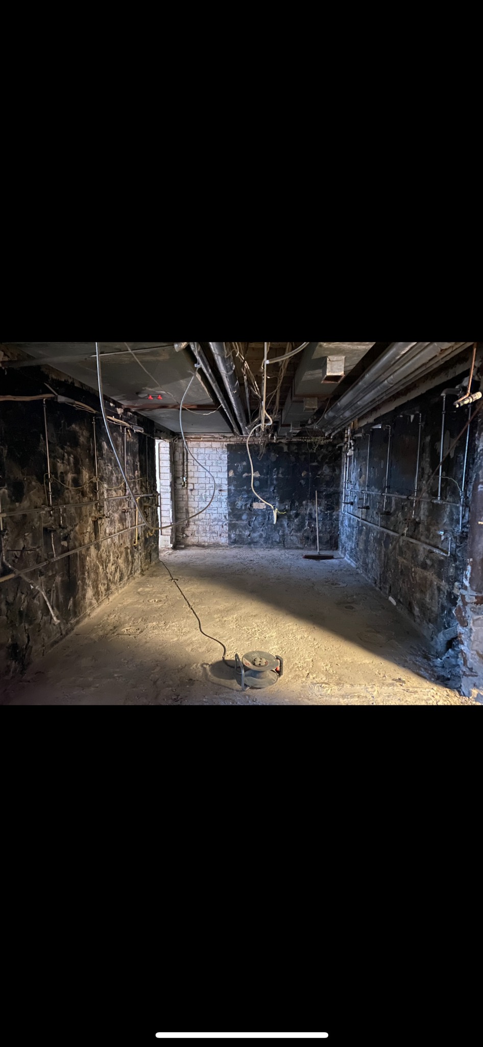 Pomieszczenie w trakcie rozbiórki, widoczne odsłonięte cegły, rury, przewody i sprzęt budowlany