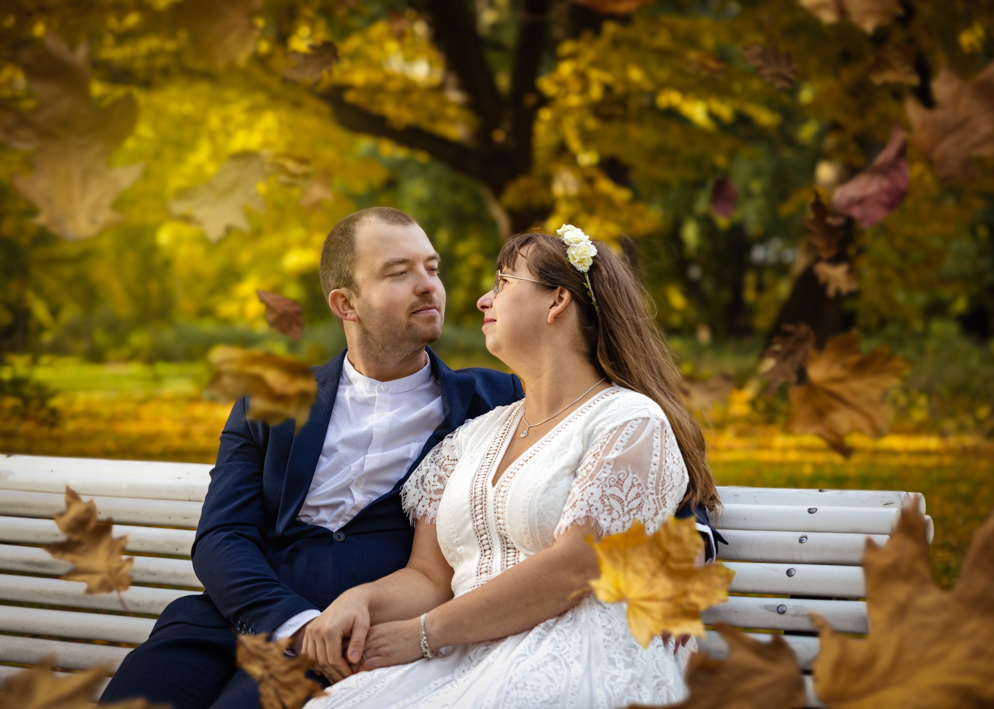 Zakochana para siedzi na ławce w parku jesienią, opadające liście dodają uroku.
