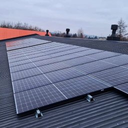 Autoryzowani PC/PV<br>Dolny Śląsk / Opolskie - Panel słoneczny zamontowany na blaszanym dachu budynku przemysłowego z pomarańczowym dachem w tle, widoczne kominy.