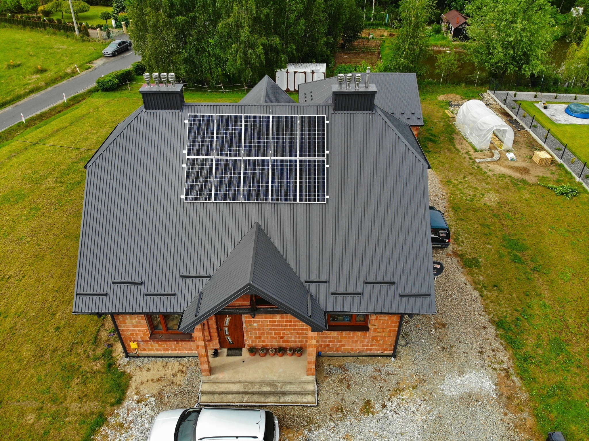 Dom jednorodzinny z szarą blachodachówką i panelami fotowoltaicznymi na dachu, widok z lotu ptaka.