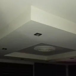 Biały sufit podwieszany z dekoracyjnym elementem centralnym i czterema punktowymi lampami LED, widoczne krawędzie i załamania konstrukcji.