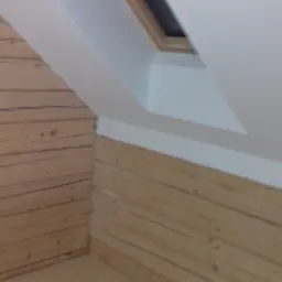 Poddasze wykończone boazerią i pomalowane na biało, z widocznym oknem dachowym w drewnianej ramie.