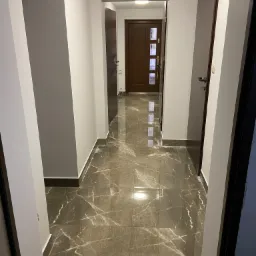 Wykończony korytarz w mieszkaniu z szarymi ścianami, ciemnymi drzwiami i podłogą z płytek imitujących marmur z wyraźnym połyskiem.