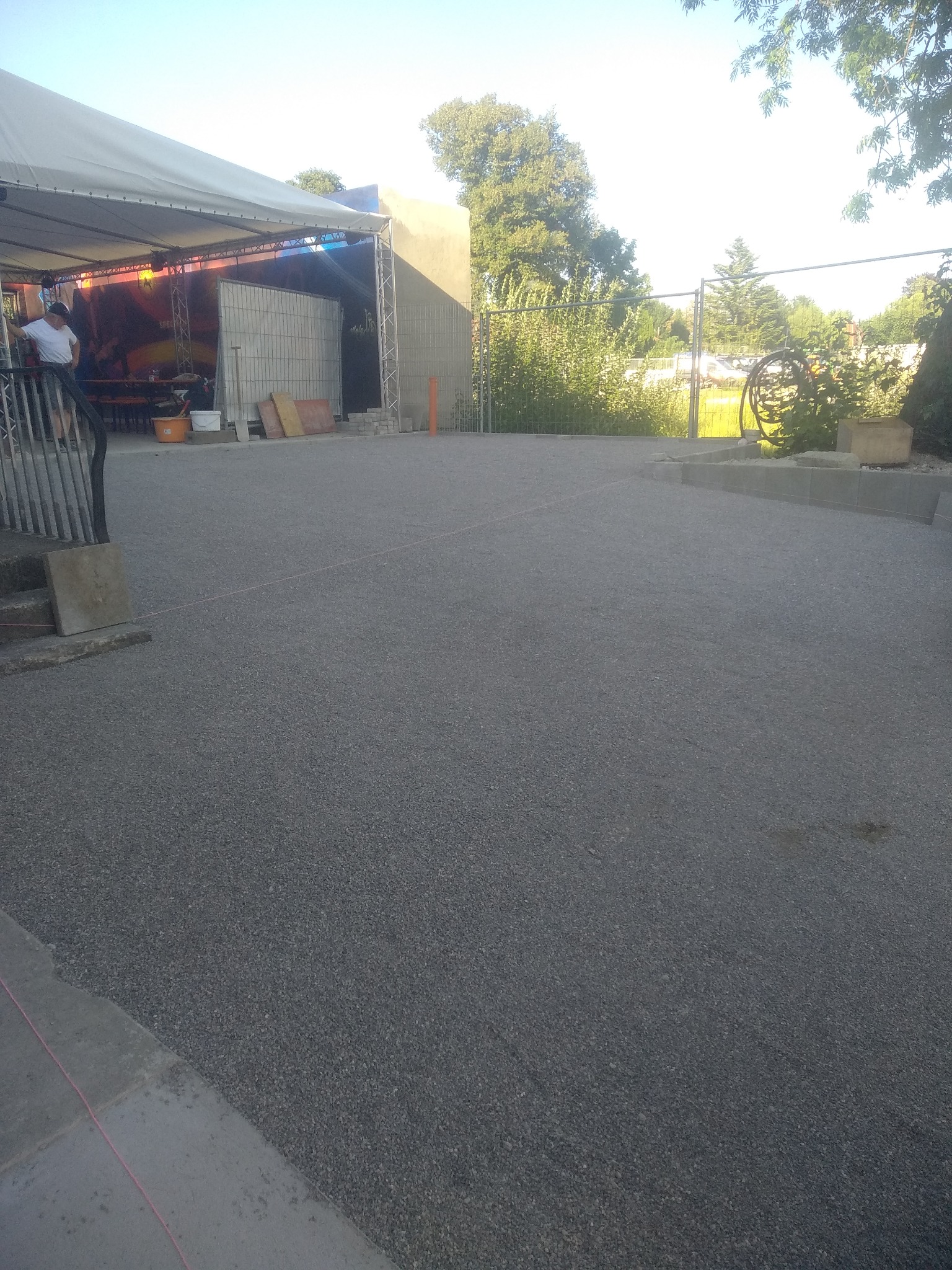 Nowa nawierzchnia z drobnego kruszywa na posesji w Gozdnie, widoczna scena z zadaszeniem w tle i barierka schodów po lewej.