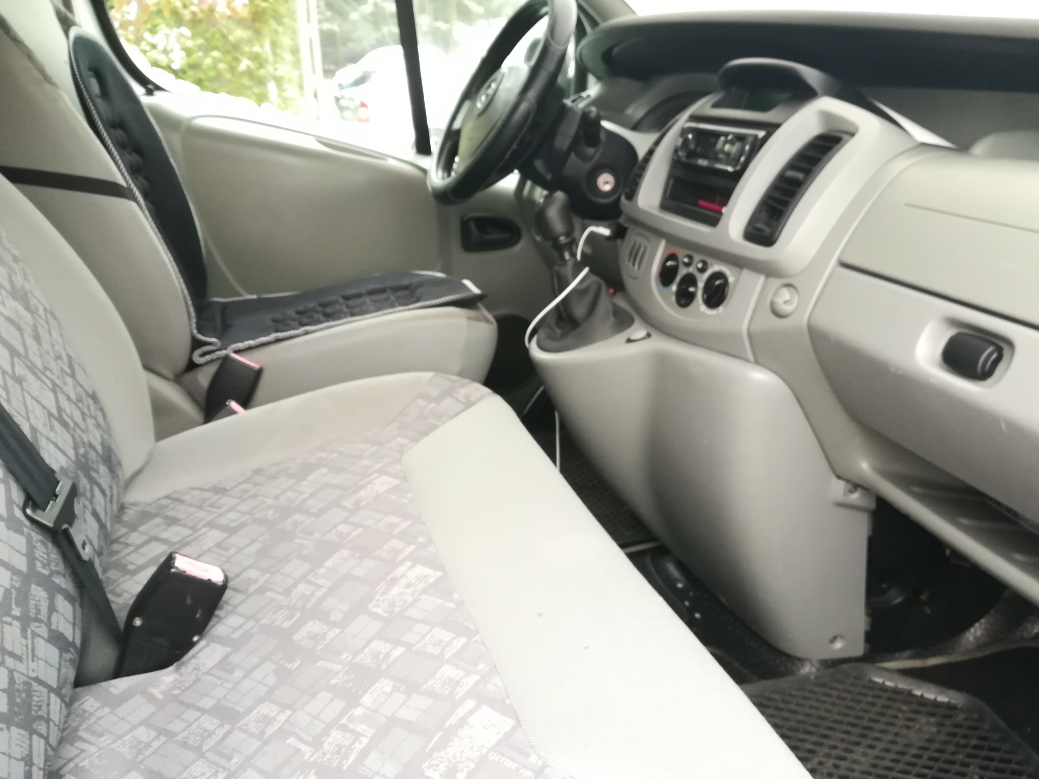 Wnętrze jasnoszarego busa z widocznymi fotelami pasażerów z wzorem w szarą kratę, deską rozdzielczą i kierownicą.