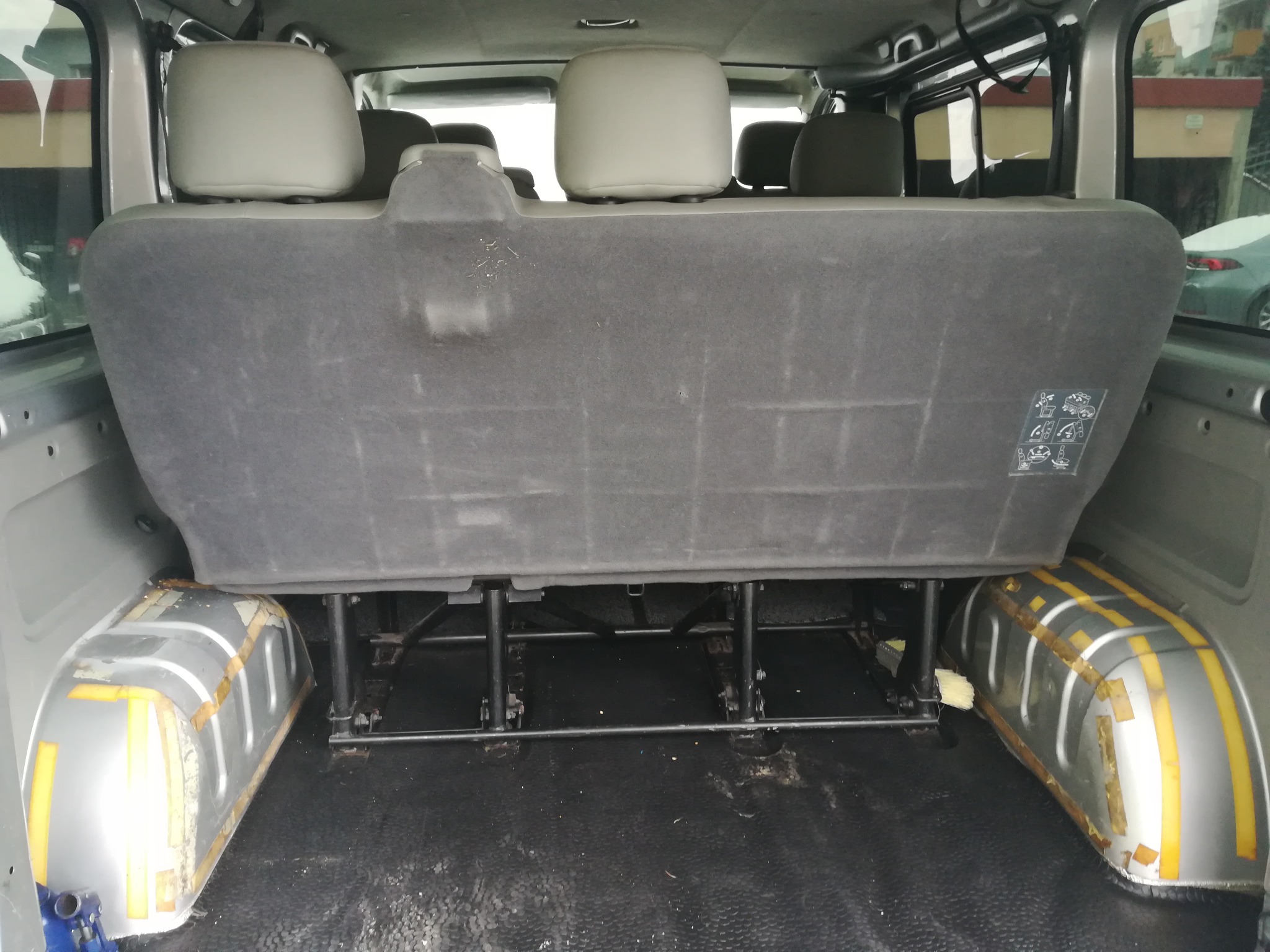Wnętrze busa z zamontowanymi szarymi siedzeniami i widocznymi elementami karoserii zabezpieczonymi taśmą malarską.