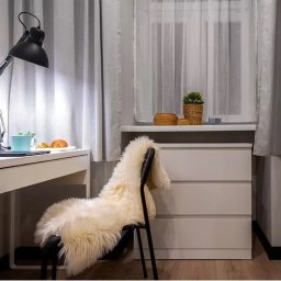 A.W. Construction Ariel Włodarczyk - Jasne wnętrze pokoju z biurkiem, lampką, krzesłem z futrzanym siedziskiem i regałem na książki, utrzymane w minimalistycznym stylu.