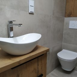 A.W. Construction Ariel Włodarczyk - Nowoczesna łazienka w odcieniach szarości z umywalką nablatową w kształcie łzy na drewnianej szafce z czarnymi uchwytami, chromowaną baterią i podwieszaną toaletą z przyciskiem spłukującym Roca.