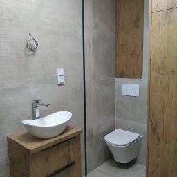 A.W. Construction Ariel Włodarczyk - Nowoczesna łazienka w odcieniach szarości i drewna z wiszącą toaletą, umywalką nablatową o owalnym kształcie na szafce z drewnianym frontem i wystającymi przewodami elektrycznymi na ścianie.