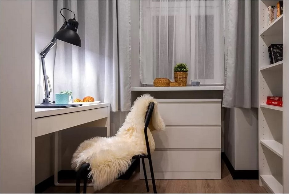 Jasne wnętrze pokoju z biurkiem, lampką, krzesłem z futrzanym siedziskiem i regałem na książki, utrzymane w minimalistycznym stylu.