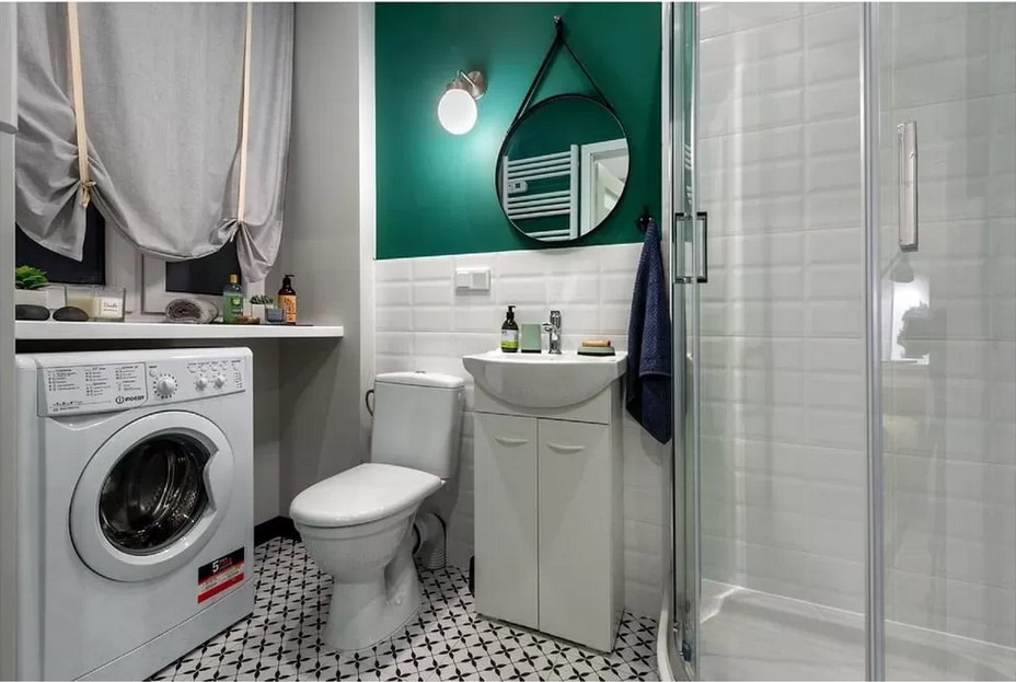Nowoczesna łazienka z białą armaturą, pralką pod blatem, kabiną prysznicową i zieloną ścianą akcentującą, uzupełniona okrągłym lustrem i czarno-białą podłogą.