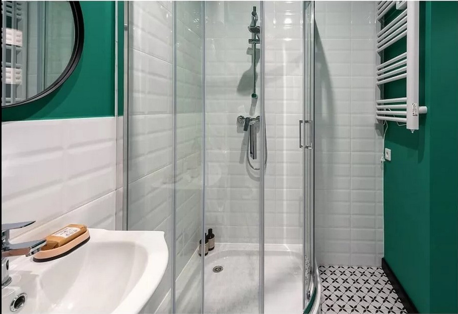 Nowoczesna łazienka z kabiną prysznicową, białą umywalką z mydłem w kostce, grzejnikiem drabinkowym i zieloną ścianą akcentującą, wykończona białymi płytkami i czarno-białą mozaiką na podłodze.
