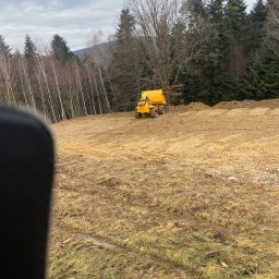 Kam-Bet - Żółta wywrotka na rozległym terenie przygotowanym do budowy, w tle las mieszany i pochmurne niebo.