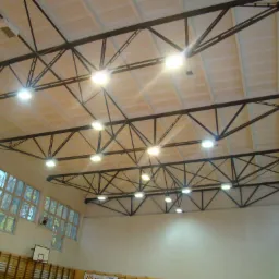 Oświetlenie LED w hali sportowej z widoczną konstrukcją stalową pod sufitem i rzędami okien po lewej stronie.