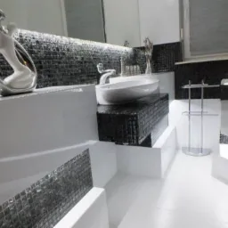 Elegancka łazienka w czarno-białej kolorystyce z mozaiką, umywalką nablatową i dekoracyjną figurką.