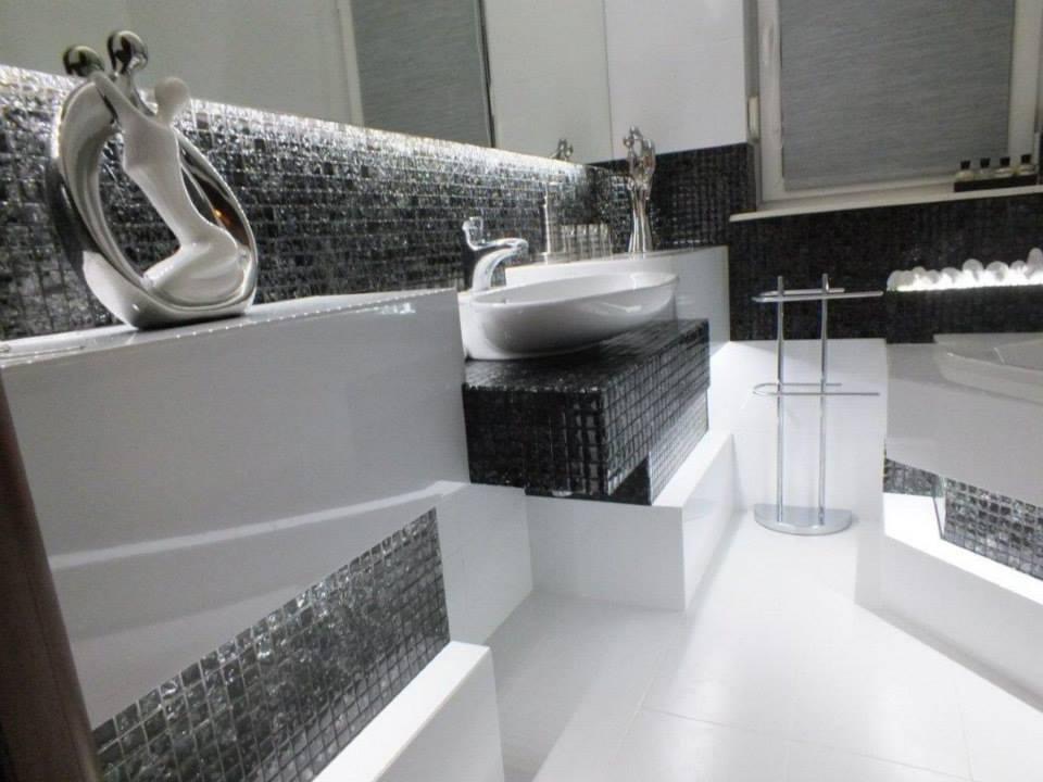 Elegancka łazienka w czarno-białej kolorystyce z mozaiką, umywalką nablatową i dekoracyjną figurką.