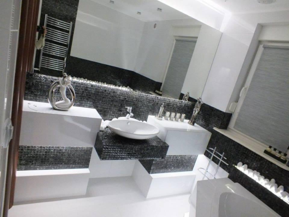 Nowoczesna łazienka z białą armaturą i czarno-białą mozaiką, nietypowa konstrukcja umywalki z podświetleniem, dekoracyjne figurki na blacie