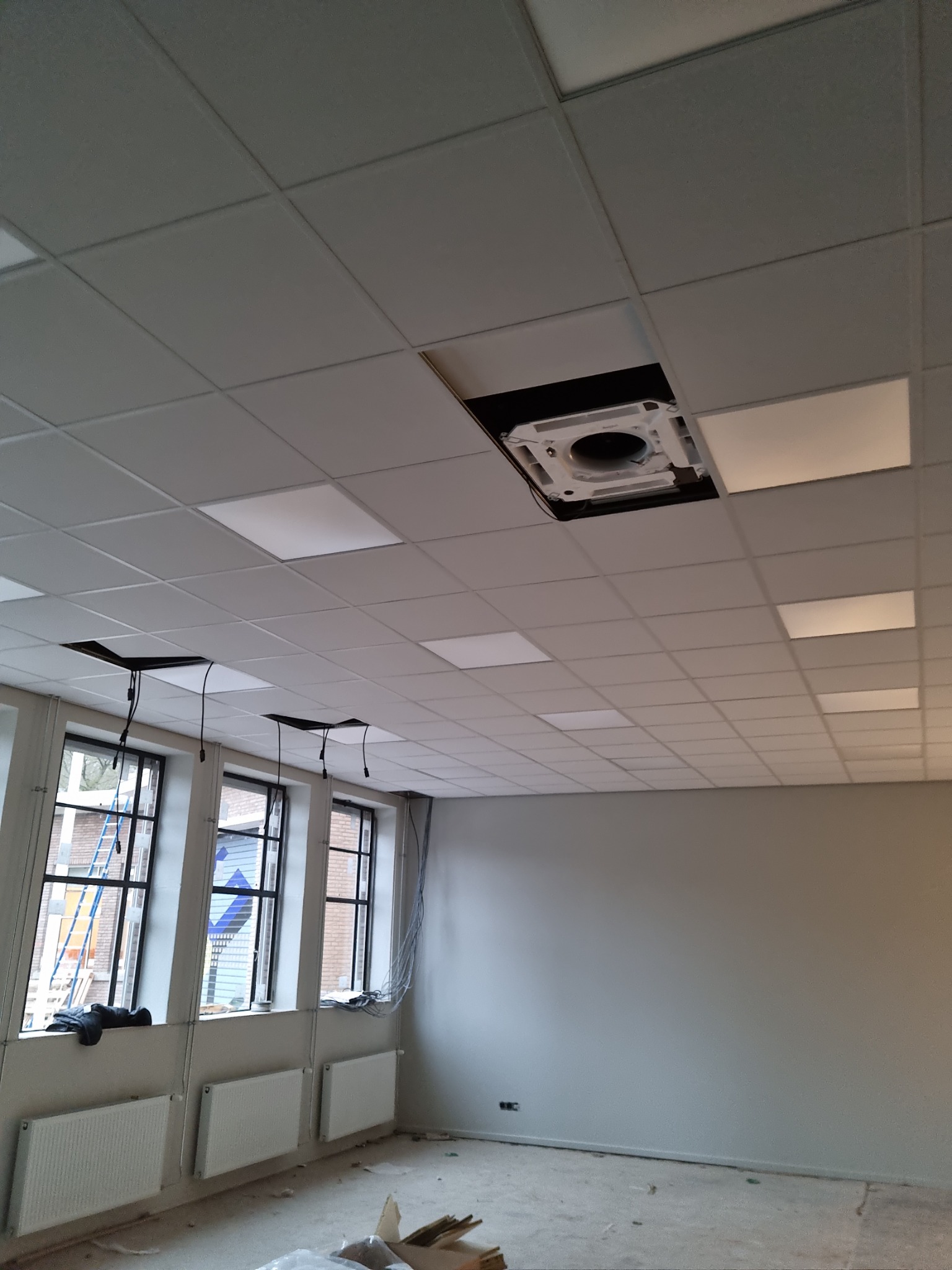 Montaż sufitu kasetonowego z wbudowanym systemem klimatyzacji w przestrzeni biurowej, widoczne kable i otwory na oświetlenie.