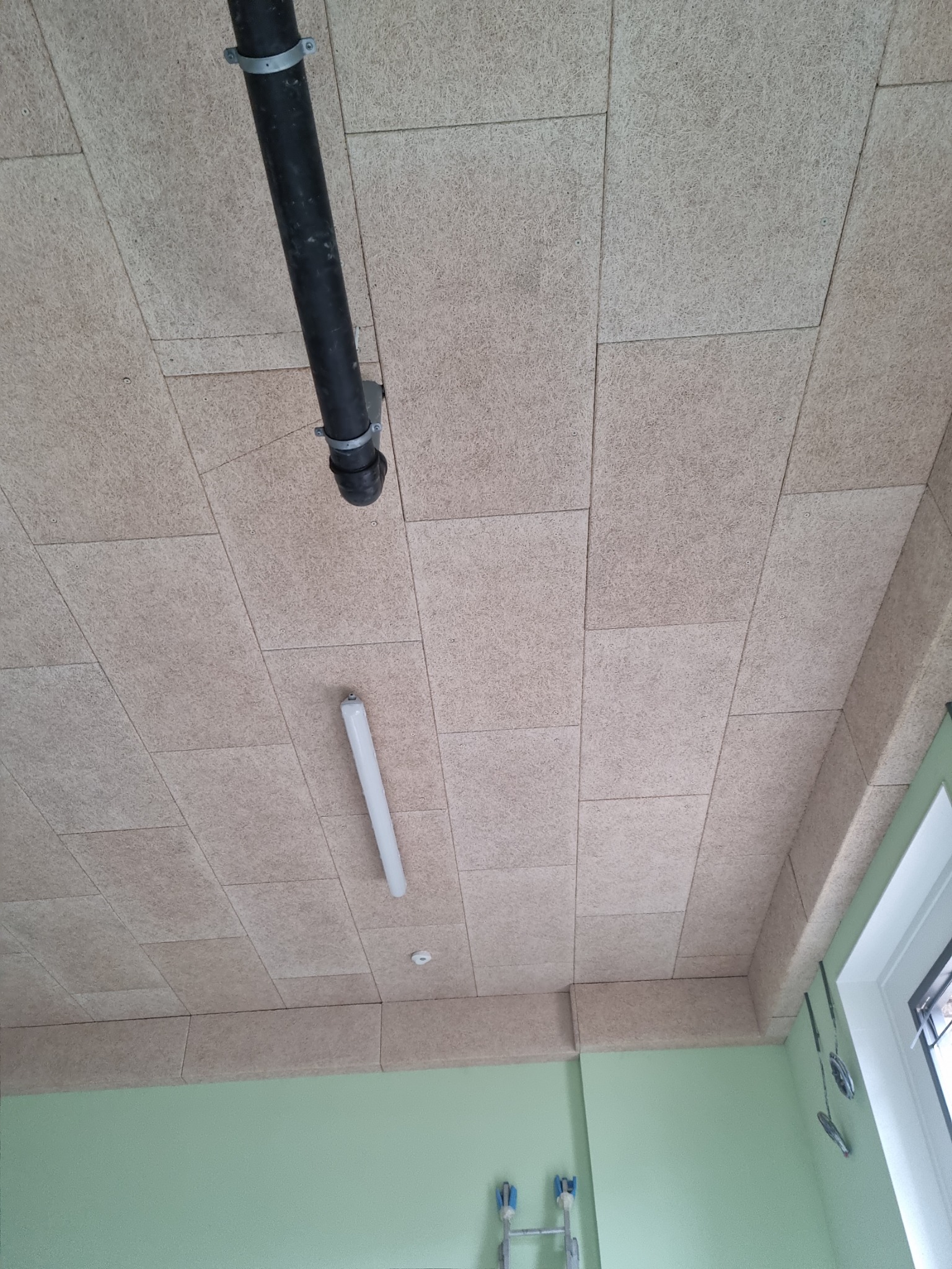 Zamontowany sufit z paneli z włókna drzewnego, widoczna instalacja rur i oświetlenie LED, ściany pomalowane na jasnozielono