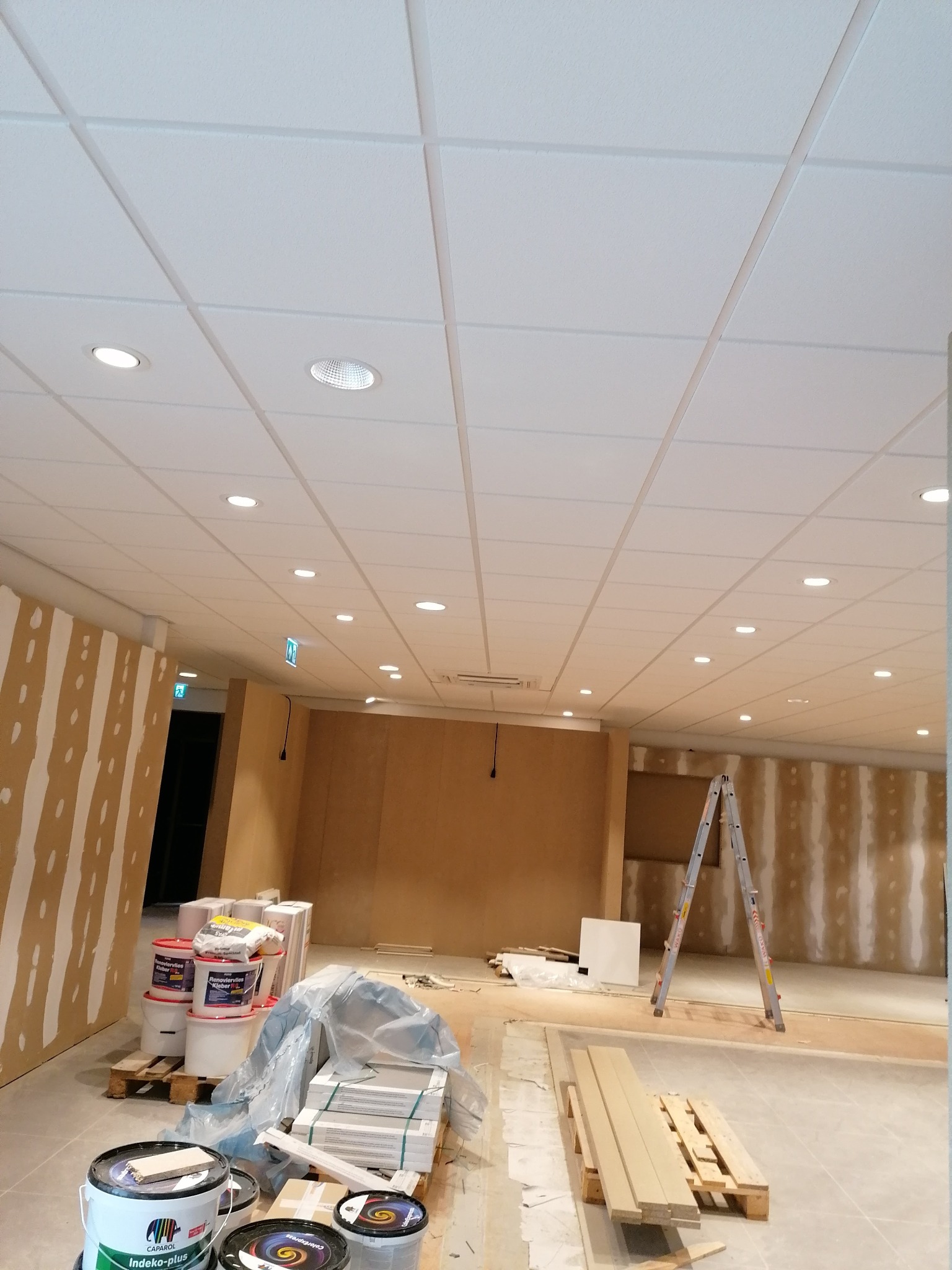 Montaż sufitu podwieszanego kasetonowego z oświetleniem LED, w tle ściany przygotowane do położenia gładzi, widoczne materiały budowlane i drabina.