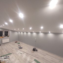 Usługi Elektryczne Radosław Dernałowicz - Pokój z szarymi ścianami i zamontowanym oświetleniem punktowym w suficie pod skosem, widoczne narzędzia i materiały budowlane na podłodze z paneli.