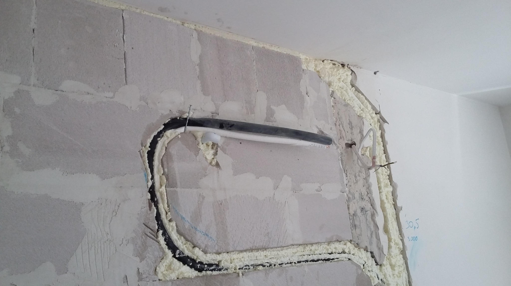 Montaż instalacji klimatyzacji w nowym budynku: czarna rura otoczona pianką montażową na surowej ścianie z widocznymi śladami po kuciu.