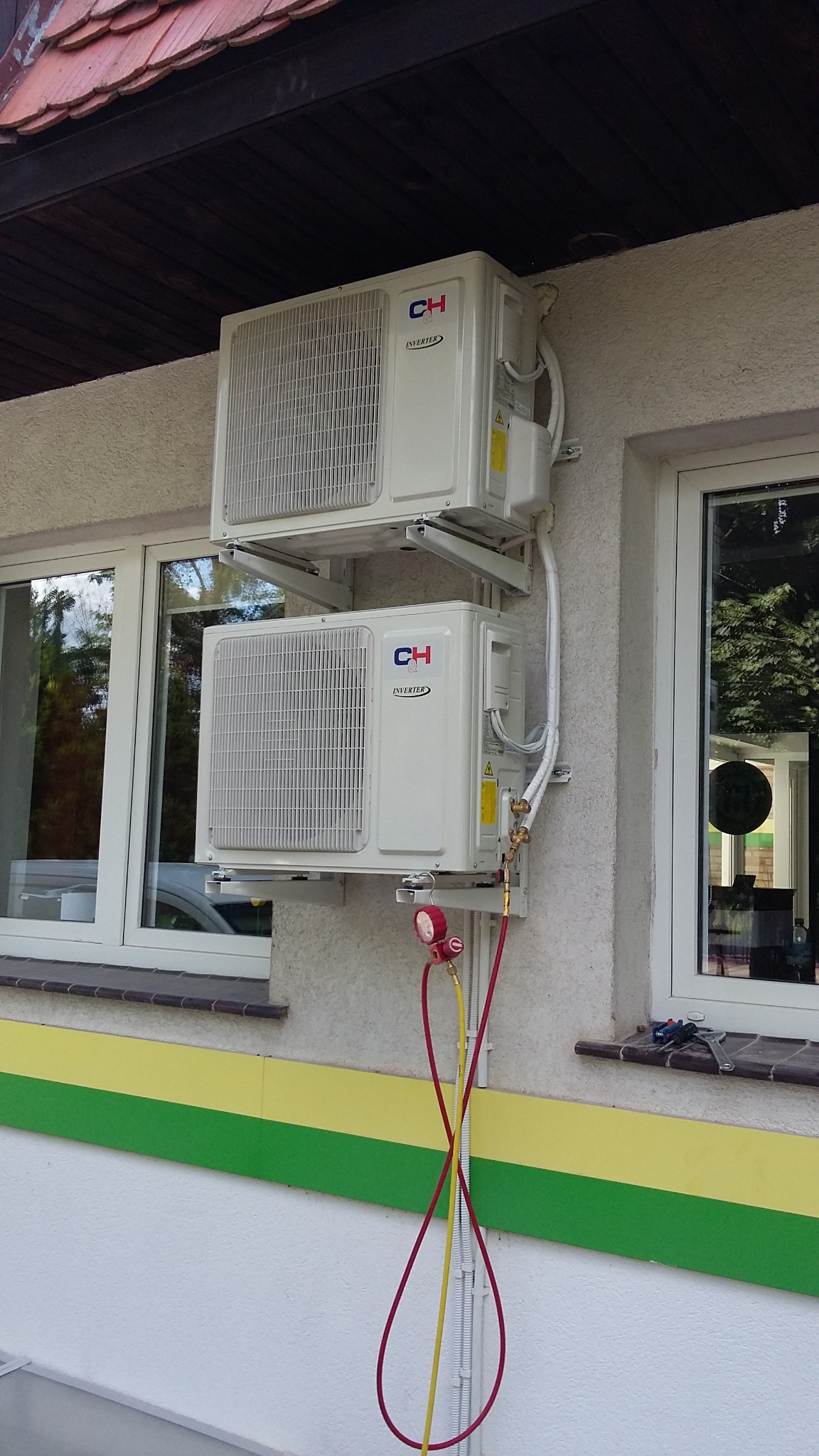 Dwa klimatyzatory marki CH zamontowane na elewacji budynku, z podłączonymi przewodami serwisowymi i manometrami, widoczne okna i narzędzia na parapecie.