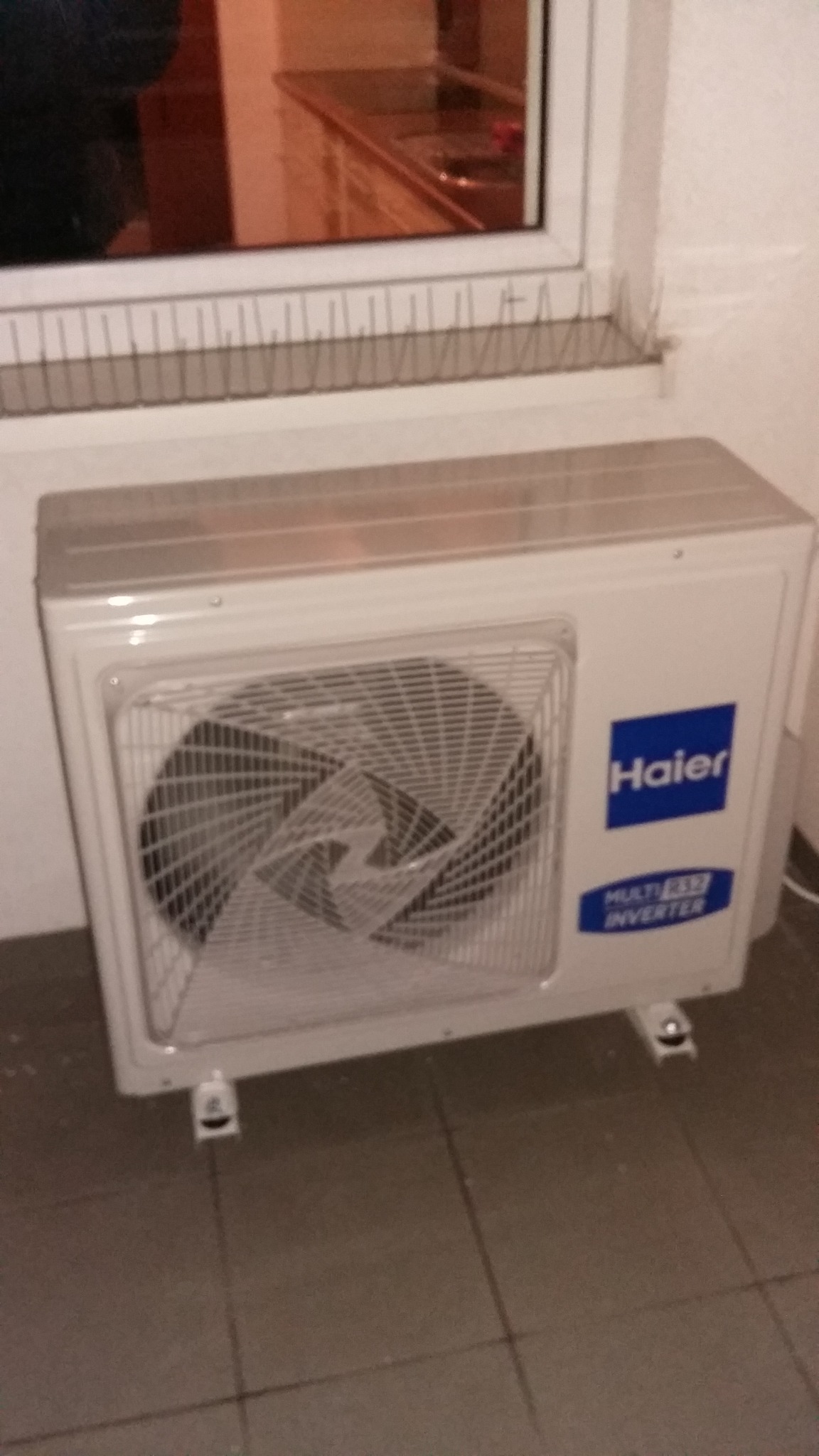 Zewnętrzna jednostka klimatyzacji Haier zamontowana na balkonie z widocznymi zabezpieczeniami przed ptakami na parapecie.