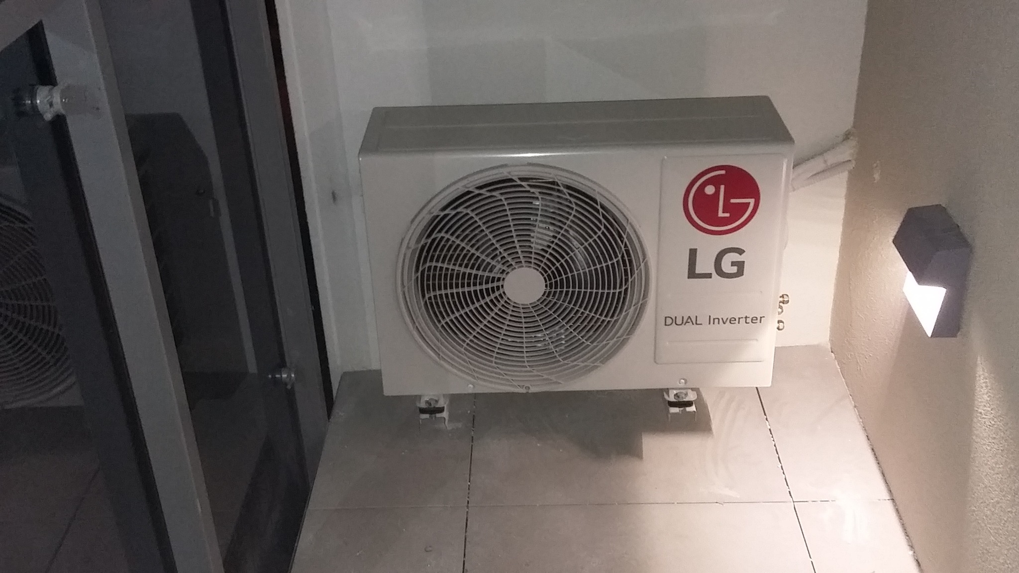 Zamontowana jednostka zewnętrzna klimatyzacji LG Dual Inverter na szarej płytce, widoczna lampka ścienna.