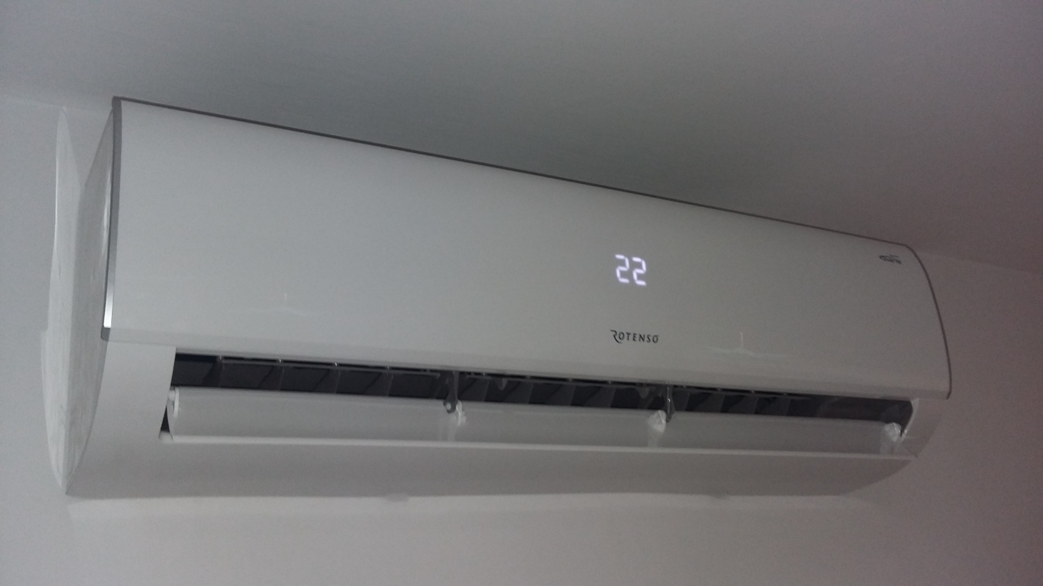 Biały klimatyzator Rotenso z wyświetlaczem temperatury ustawionym na 22 stopnie Celsjusza, zamontowany na jasnej ścianie.