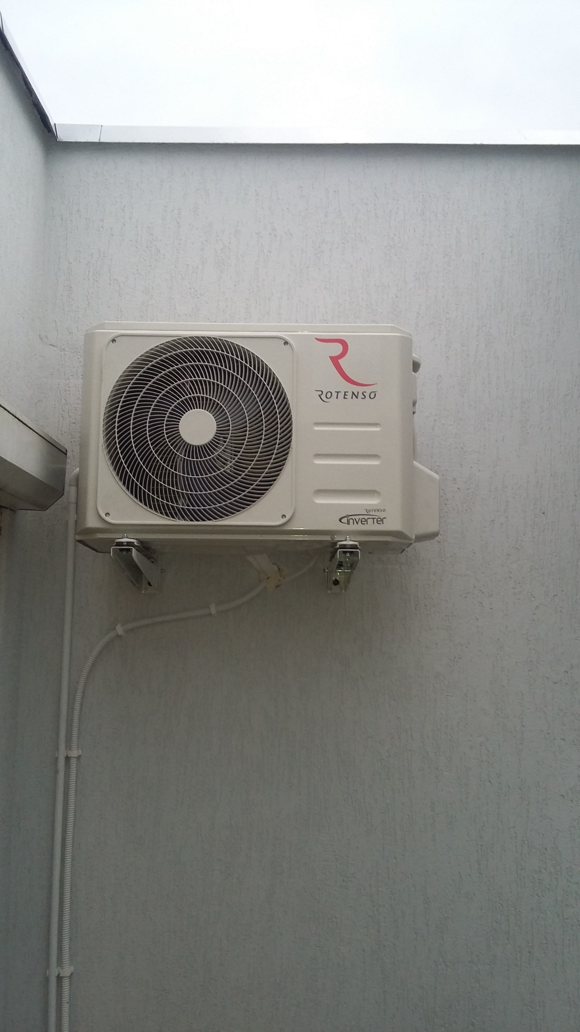 Zewnętrzna jednostka klimatyzacji Rotenso Inverter zamontowana na szarej, teksturowanej ścianie budynku, widoczne przewody w białej listwie.