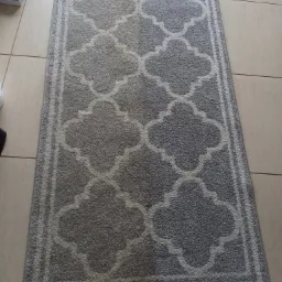 Szary dywan z wzorem marokańskim na beżowych płytkach podłogowych, obok widoczny wąż od odkurzacza i pudełko z rękawiczkami.