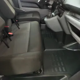 Wnętrze kabiny busa po czyszczeniu: widoczne czarne gumowe dywaniki z wytłoczonym wzorem, szare fotele z podłokietnikami i czerwonymi elementami pasów bezpieczeństwa, oraz deska rozdzielcza...