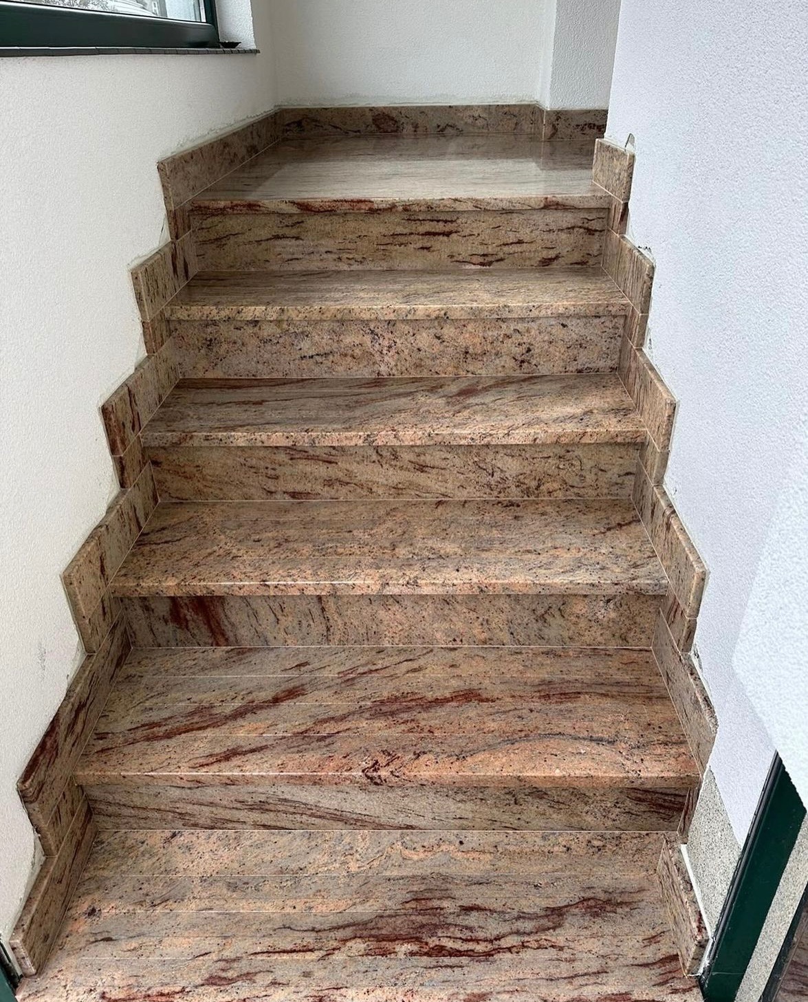 Granitowe schody wewnętrzne z charakterystycznym wzorem w odcieniach beżu i czerwieni, wykończone przy ścianie, widok z góry.