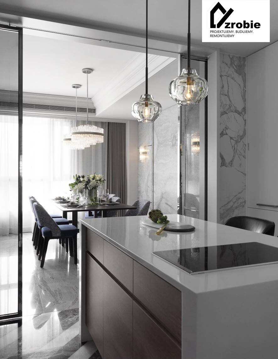 Nowoczesna kuchnia z wyspą i marmurową ścianą, oświetlona szklanymi lampami wiszącymi i kryształowym żyrandolem nad stołem jadalnym z ciemnymi krzesłami.