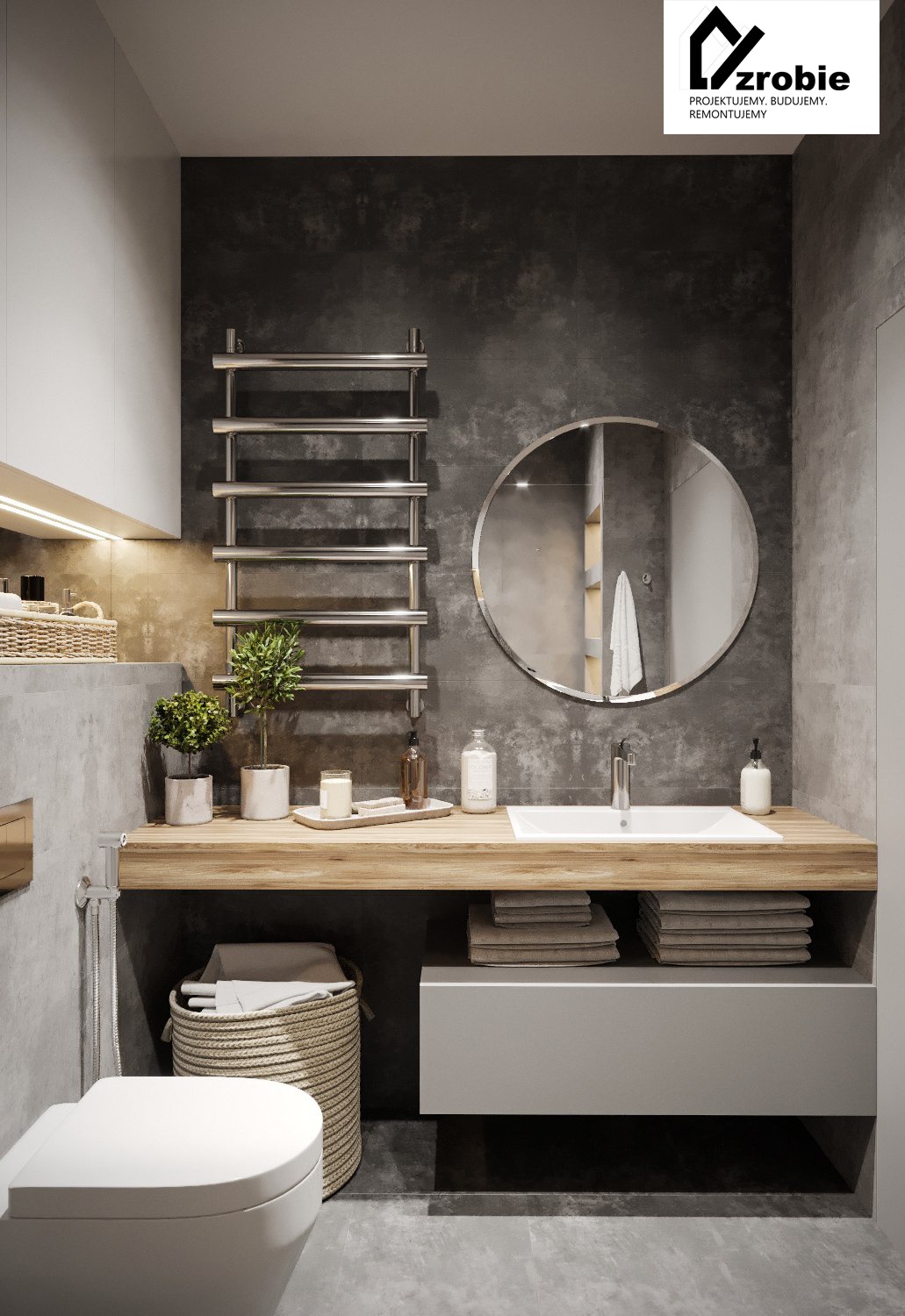 Nowoczesna łazienka w odcieniach szarości z drewnianym blatem, okrągłym lustrem i grzejnikiem drabinkowym. Na blacie dekoracje: świeca, rośliny w doniczkach i dozowniki. Pod blatem kosz na pranie...