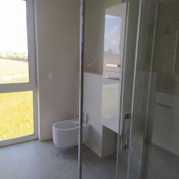 GranPlus Dmytro Libeha - Jasna łazienka z kabiną prysznicową ze szkła hartowanego, białym bidetem i widokiem na łąkę za oknem.