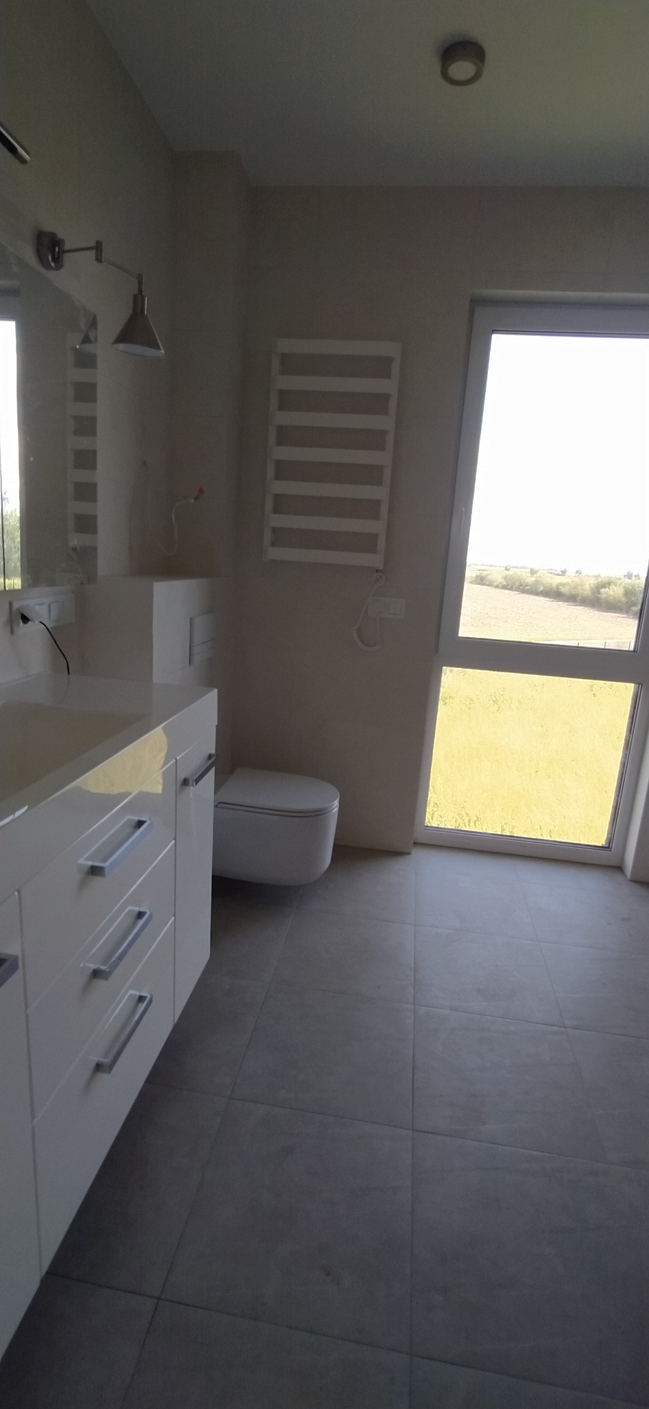 Nowoczesna łazienka z białymi meblami, grzejnikiem drabinkowym i dużym oknem z widokiem na zieleń.