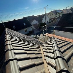 PL DACH Patryk Lake Ciesielstwo-Dekarstwo - Nowe, brązowe dachówki ceramiczne ułożone na dachu domu jednorodzinnego w słoneczny dzień, widoczne elementy montażowe i fragment rusztowania.