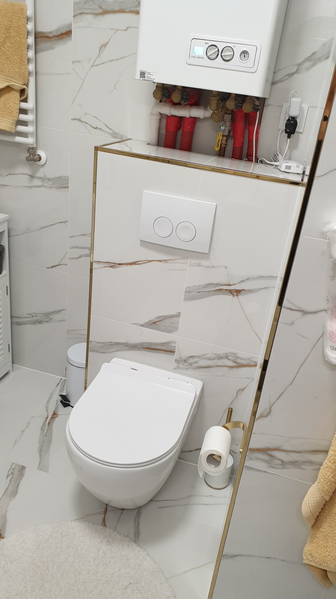 Nowoczesna toaleta wisząca z marmurowymi płytkami, złotymi akcentami i piecem gazowym nad spłuczką.