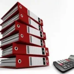 Stos czerwonych segregatorów z dokumentami, obok kalkulator biurowy na białym tle.