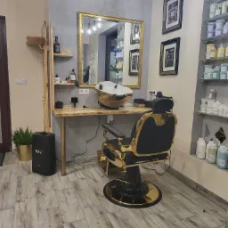 Wnętrze salonu fryzjerskiego z złotym fotelem barberskim, umywalką w kolorze złota, lustrem w złotej ramie, półkami z kosmetykami i podłogą imitującą drewno.