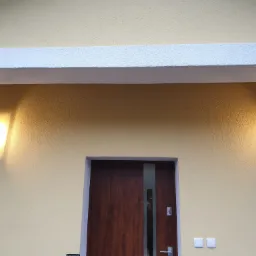 Elewacja budynku z drewnianymi drzwiami z pionowym przeszkleniem i symetrycznie umieszczonymi, nowoczesnymi lampami ściennymi o kwadratowym kształcie, oświetlającymi żółtą, teksturowaną ścianę.