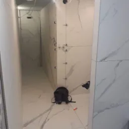 Układanie płytek imitujących marmur w łazience w Koszalinie, widoczne krzyżyki dystansowe, instalacja elektryczna i torba narzędziowa na podłodze.